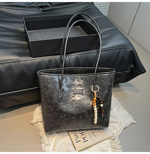 Detail of black leather tote bag with heart and dog embossed patterns and beaded charm