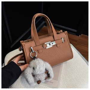 Macro view of brown lychee grain leather tote bag with silver lock and plush rabbit charm