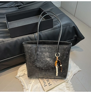 Detail of black tote bag featuring embossed leather texture and colorful bead charm