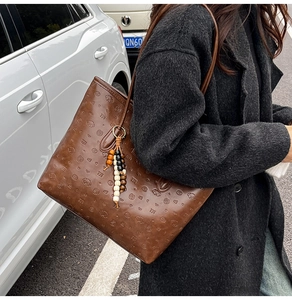 Detail of dark brown tote bag with embossed cartoon patterns and colorful beaded charm