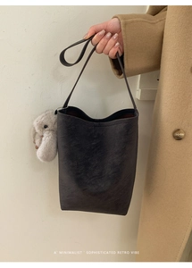 Detail of grey retro bucket bag with plush rabbit charm held by model in wool coat