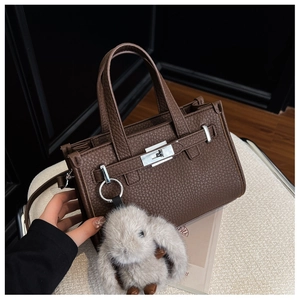 Close-up of brown litchi grain leather bag with silver buckle and plush rabbit charm