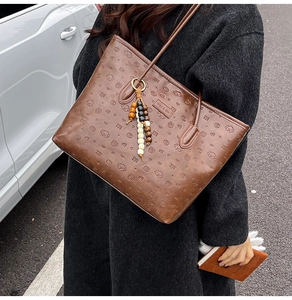 Close-up of a brown embossed tote bag with puppy patterns and a beaded charm on a model