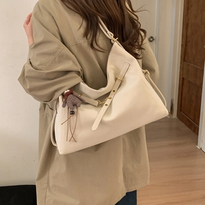Detailansicht der cremefarbenen Oversized-Tasche mit Zierriemen und süßem Teddybär-Anhänger