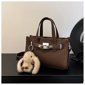 Detail of dark brown lychee leather tote bag with silver lock and plush rabbit charm