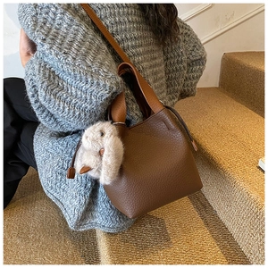 Détail du sac seau en cuir marron foncé avec texture lychee et breloque lapin en peluche
