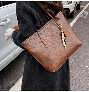 Detail of dark brown embossed leather tote bag with dog patterns and beaded tassel charm