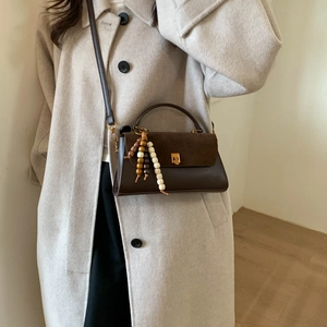 Détail du sac bandoulière marron foncé avec pompon en perles de bois et boucle en métal