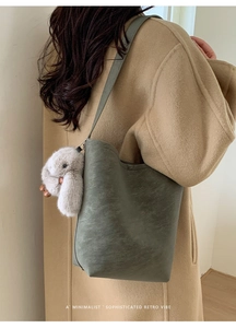Detail of dark green matte bucket bag with a gray plush bunny charm on a wool coat