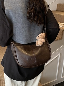 Brown faux leather half-moon hobo bag with teddy charm on model in minimalist setting