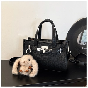 Detail of black pebbled leather tote bag with silver lock and plush bunny charm