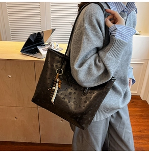 Macro shot of black embossed leather tote bag with stylish bead charm and soft texture