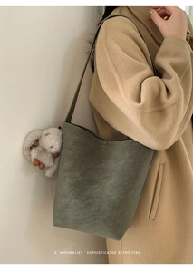 Retro grey-green bucket bag with plush rabbit charm worn over a long khaki coat