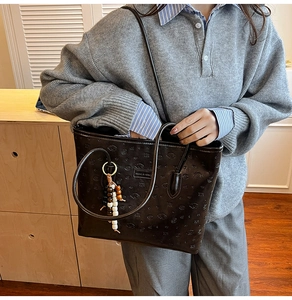 Detail of a dark brown embossed leather tote bag with unique cartoon patterns and beaded charm