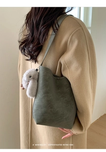 Detail of dark green bucket bag with a cute plush rabbit pendant on a long strap