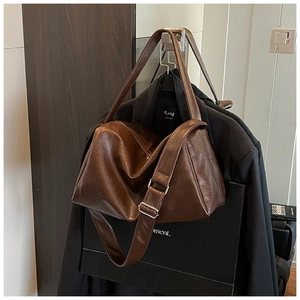 Detail der dunkelbraunen Ledertasche mit breitem Gurt und Schnalle auf schwarzem Anzug