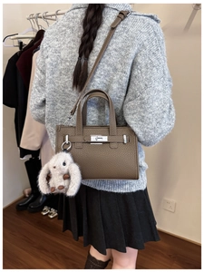 Detail of a dark brown lychee leather tote bag with a cute plush rabbit charm on a model