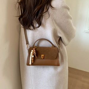 Détail d'un sac bandoulière marron avec rabat en daim et breloque en perles de bois