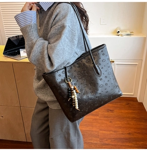Detail of black leather tote bag with embossed cartoon puppy patterns and beaded charm