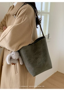 Detail view of a retro olive green bucket bag with a plush rabbit charm on a model