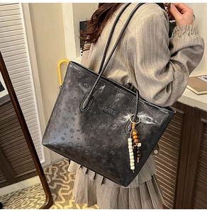 Close-up of black embossed leather tote bag with cartoon dog patterns and bead charm