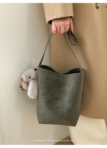 Detailed view of sage green bucket bag with a plush rabbit charm held by model