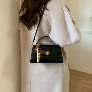 Détail d'un sac à bandoulière noir avec fermoir doré et pendentif en perles de bois