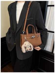 Close-up of brown litchi pattern leather bag with silver buckle and plush rabbit charm