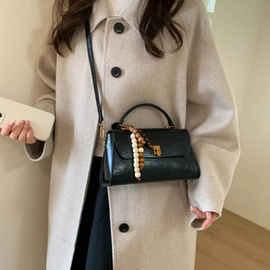 Gros plan du sac bandoulière en cuir noir avec boucle dorée et pendentif perlé rétro