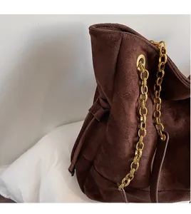 Gros plan sur un sac seau en daim marron avec détails de bandoulière en chaîne dorée