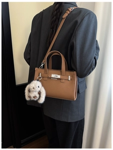Detail of a brown lychee pattern leather tote bag with metal lock and cute rabbit charm