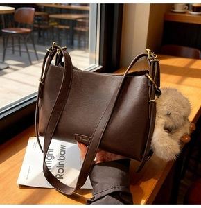 Detail of dark brown vintage underarm bag with gold hardware and plush charm on table