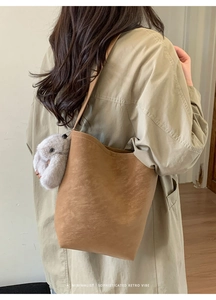 Detail view of brown suede bucket bag with wavy rim and plush rabbit keychain accessory