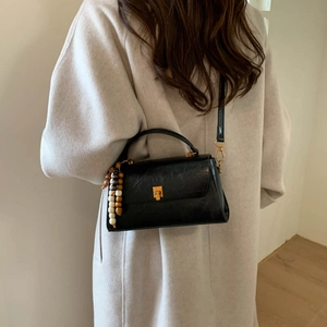 Détail d'un sac bandoulière trapèze noir chic avec gland en perles colorées et boucle dorée