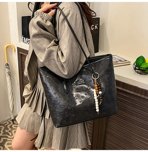 Detail of black embossed tote bag featuring dog patterns and bohemian wooden bead charm