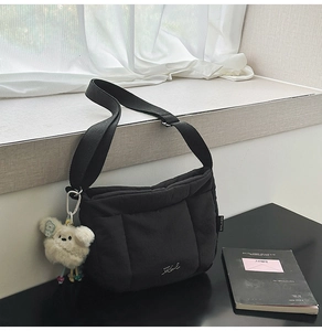 Détail du sac seau matelassé noir avec bandoulière réglable et pendentif en peluche