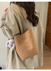 Brown suede bucket bag with a plush rabbit charm shown on a khaki trench coat