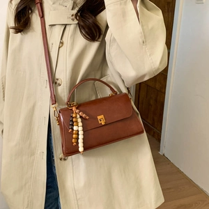 Sac bandoulière en cuir marron avec verrou doré et gland en perles sur manteau beige