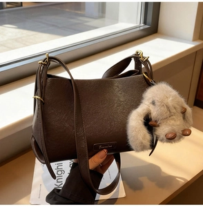 Detail of dark brown leather handbag with a plush rabbit charm and gold metal buckle