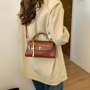 Détail d'un sac bandoulière marron avec pendentif en perles de bois sur blazer beige