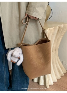 Detail of retro brown bucket bag with a plush rabbit charm and smooth matte texture