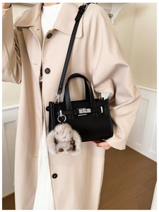 Detail of black pebbled leather tote with silver lock and plush bunny charm accessory