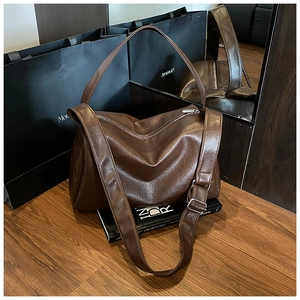 Nahaufnahme einer großen dunkelbraunen Ledertasche mit breitem Schultergurt auf Holzboden