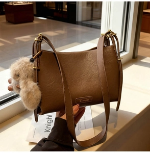Detail of brown litchi pattern leather shoulder bag with a cute plush bunny charm