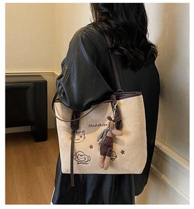 Detail of beige suede tote bag with cartoon cat embroidery and cute plush bunny charm