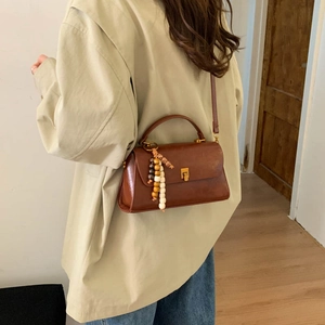 Détail d'un sac à main en cuir marron avec fermoir doré et perles décoratives en bois