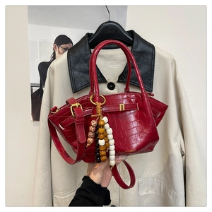 Dettaglio di una borsa a secchiello rossa coccodrillo con nappa di perle e logo oro