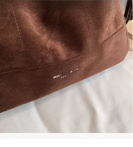 Détail d'un sac à bandoulière en daim marron foncé avec surpiqûres et logo imprimé