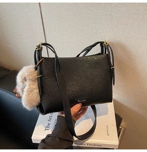 Close-up of black textured leather shoulder bag with gold buckle and plush rabbit charm