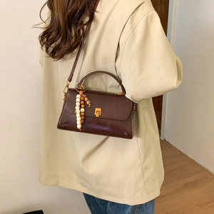 Détail d'un sac bandoulière marron vintage avec boucle dorée et pendentif en perles